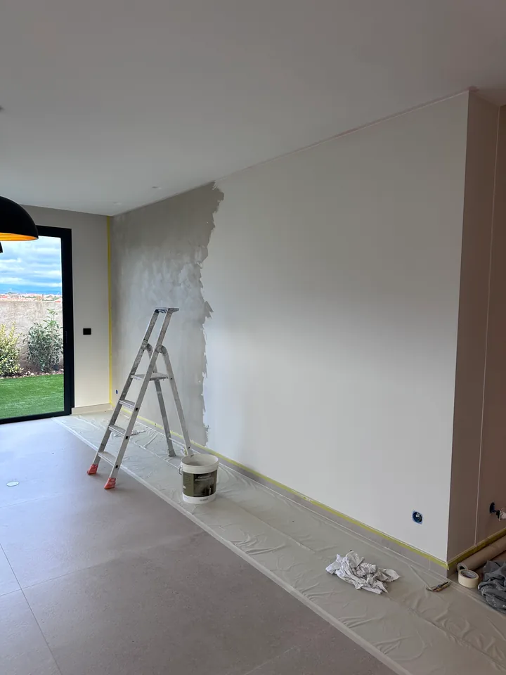 Mur à moitié recouvert d'un enduit décoratif Marmorino en cours d'application, sol protégé par une bâche et ruban de masquage en pied de mur