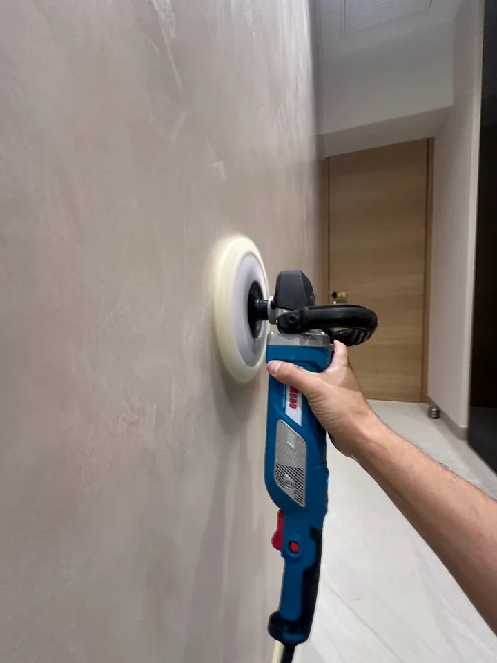 Lustrage d'un mur en Marmorino à la machine : disque de polissage tenu à la main sur une surface satinée beige