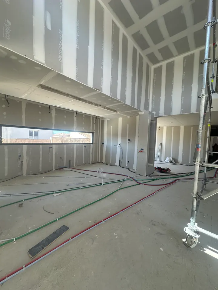 Cuisine avant travaux sous haut plafond : murs et plafond en plaques de plâtre aux joints apparents, gaines au sol et fenêtre en bandeau