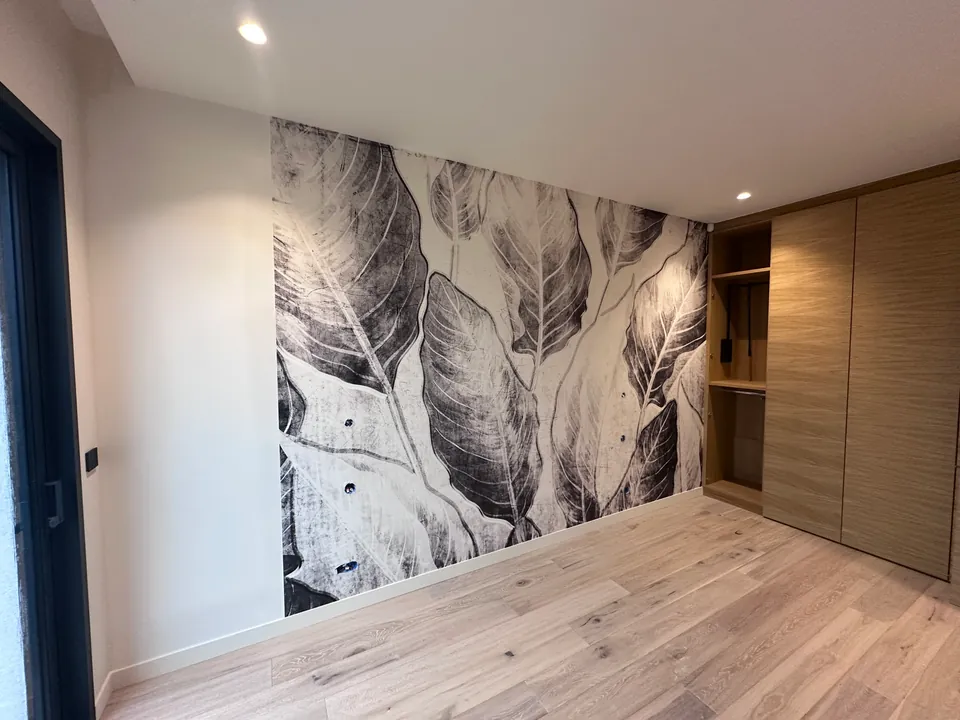 Pièce avec un papier peint panoramique à grands feuillages gris et blancs, placards en bois et parquet clair
