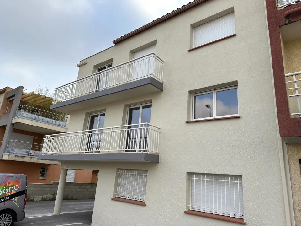 Façade de l'immeuble rénové : balcons à garde-corps blancs et sous-faces grises, enduit beige clair, fenêtres à volets roulants