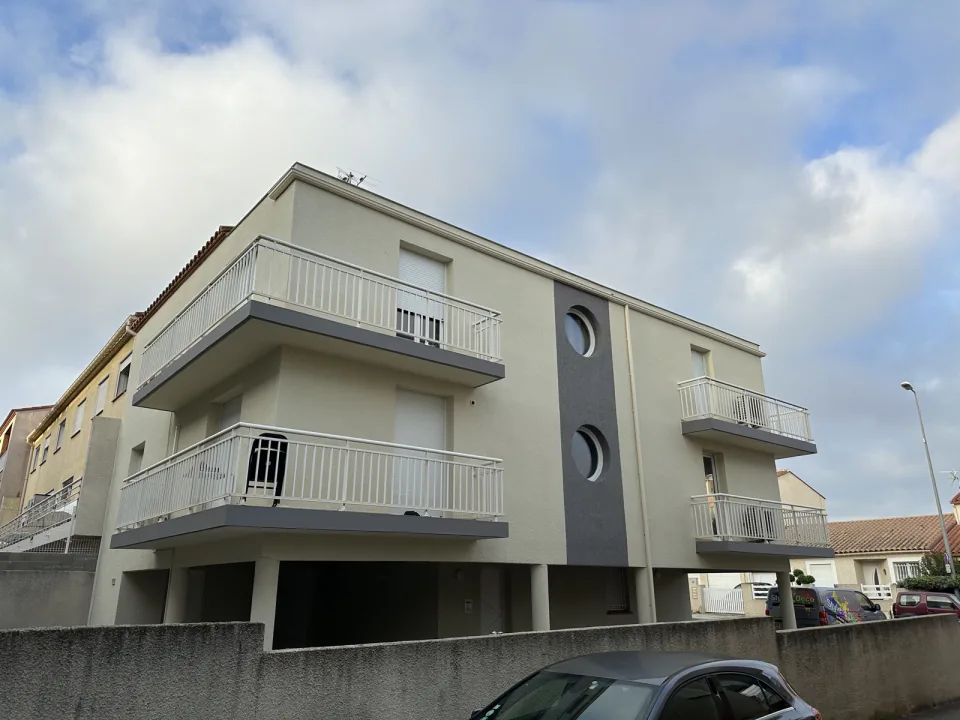 Immeuble résidentiel de trois niveaux à Perpignan après ravalement : façades beige clair, bande grise percée de deux hublots et balcons à garde-corps blancs